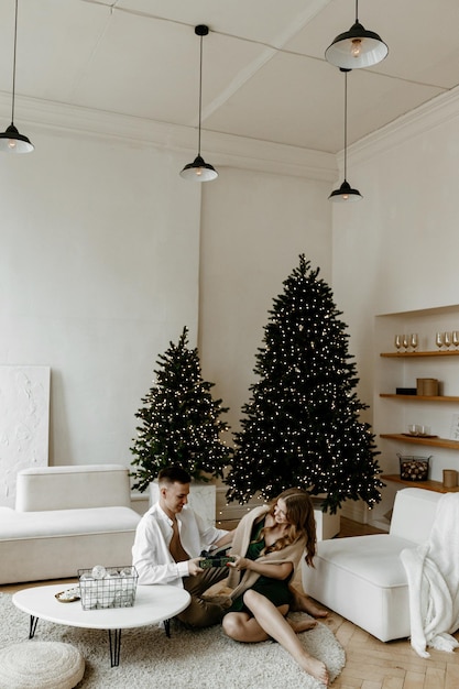 Beautiful young couple exchanging Christmas gifts at home in a bright living room