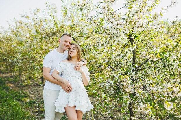 A beautiful young couple expecting a pregnancy in a romantic place a spring blossoming apple orchard Happy joyful couple enjoying each other while walking in the garden A man holds a woman's hand