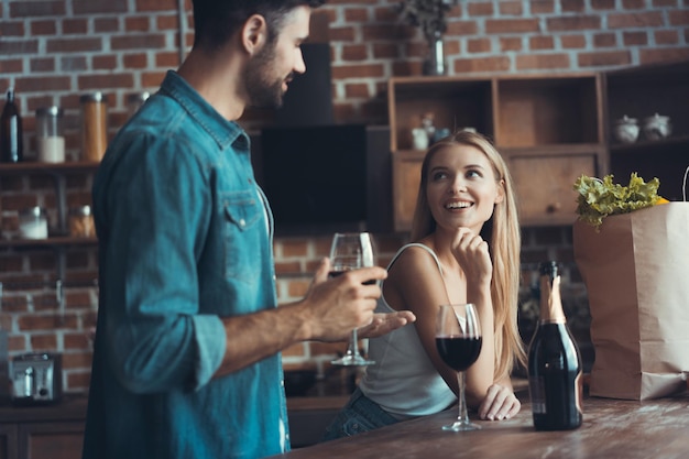 Beautiful young couple is drinking wine and smiling while cooking in kitchen at home