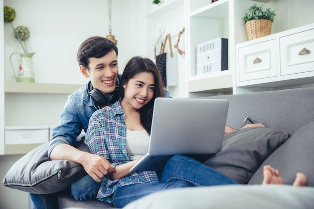 Beautiful young couple is feeding smiling while using notebook watch movie in living room