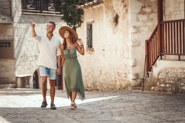 A beautiful young couple is having fun while walking around a Mediterranean town. They are enjoyed in summer sunny day, holding each other's hand and smiling.