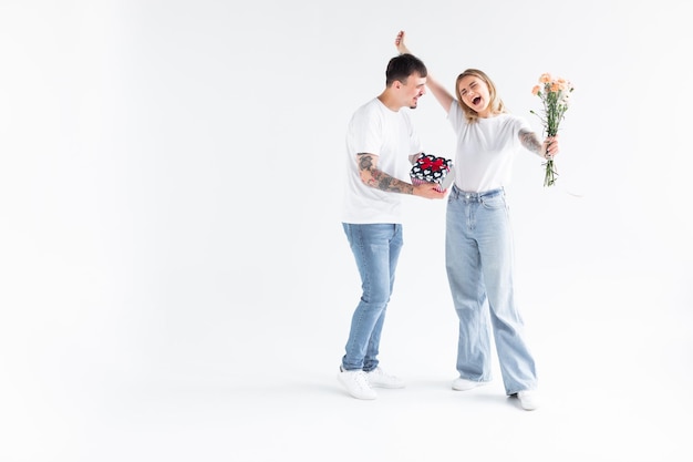 Beautiful young couple in love at home celebrating with a gift box and flower exchange