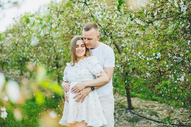 Beautiful young couple man and pregnant woman in spring garden Beauty lifestyle family concept A happy mother is expecting a baby A happy young couple in a blooming garden