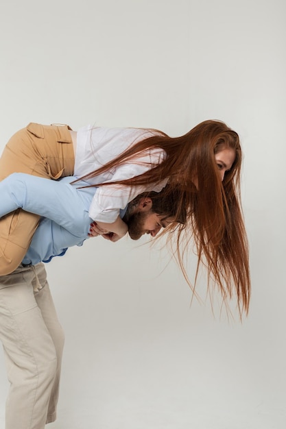 Beautiful young couple man and redheaded girl fooling around and having fun on a white background in the studio Woman on a guy's back