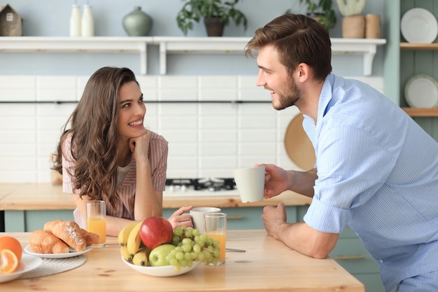 Beautiful young couple in pajamas is looking at each other and smiling while cooking in kitchen at home.