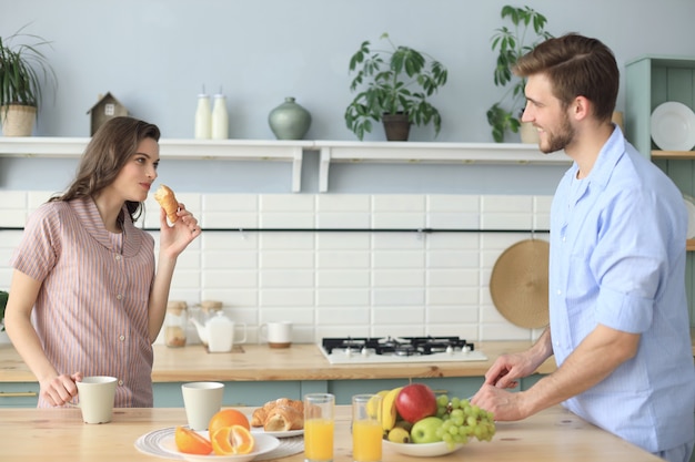 Beautiful young couple in pajamas is looking at each other and smiling while cooking in kitchen at home.