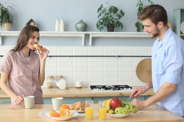 Beautiful young couple in pajamas is looking at each other and smiling while cooking in kitchen at home.