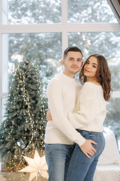 Beautiful young couple posing to photographer at new year studio christmas tree snow outside