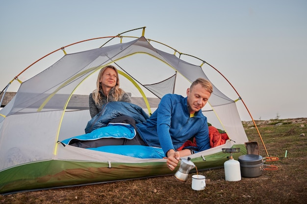 Beautiful young couple resting in camp tent and drinking tea