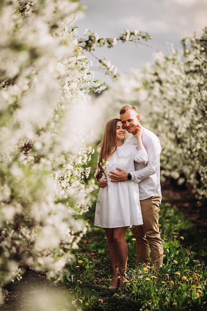 Beautiful young couple in a romantic place, spring blooming apple orchard. Happy joyful couple enjoy each other while walking in the garden. Man holding woman's hand