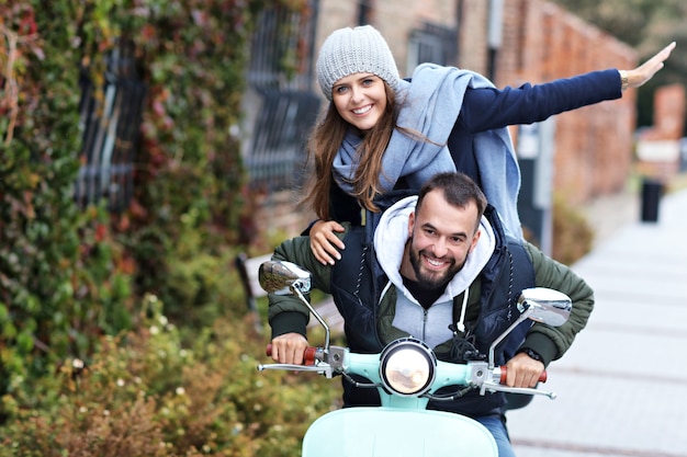 beautiful young couple smiling while riding scooter in city in autumn