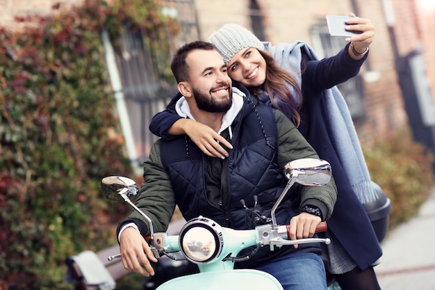 beautiful young couple smiling while riding scooter in city in autumn