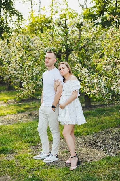 Beautiful young couple in spring garden Beauty lifestyle family concept A happy mother is expecting a baby A happy young couple in a blooming garden