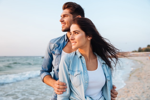 Beautiful young couple standing and looking at waves on the beach