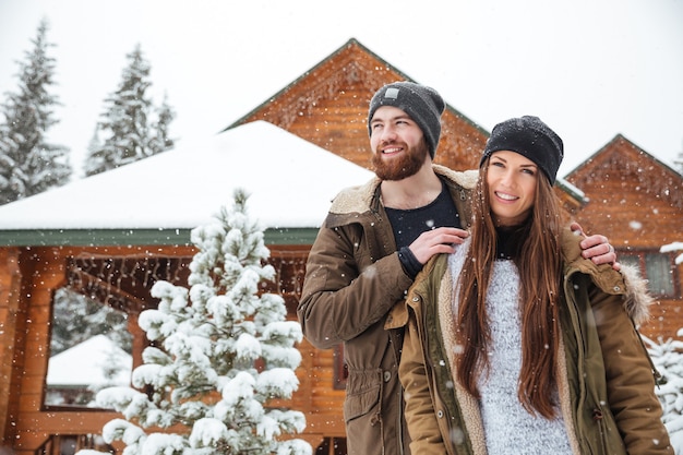 Beautiful young couple standing near log cabin in snowy weather