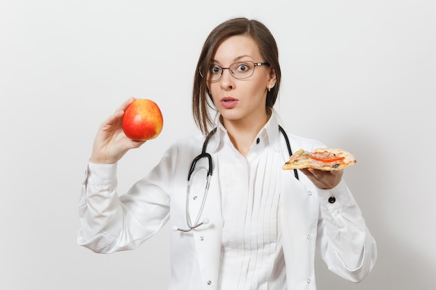 Beautiful young doctor woman with stethoscope isolated on white background. Female doctor in medical gown holding red apple piece of pizza. Healthcare personnel health concept Choice proper nutrition.