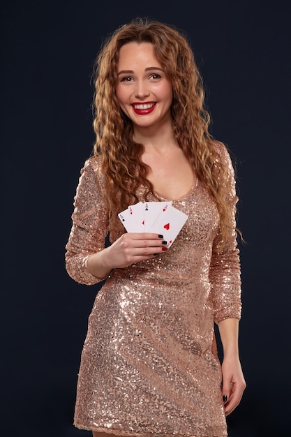 Beautiful young emotional woman in cocktail dress showing her cards to opponent, four of aces, best hand. Blcak background, studio shot