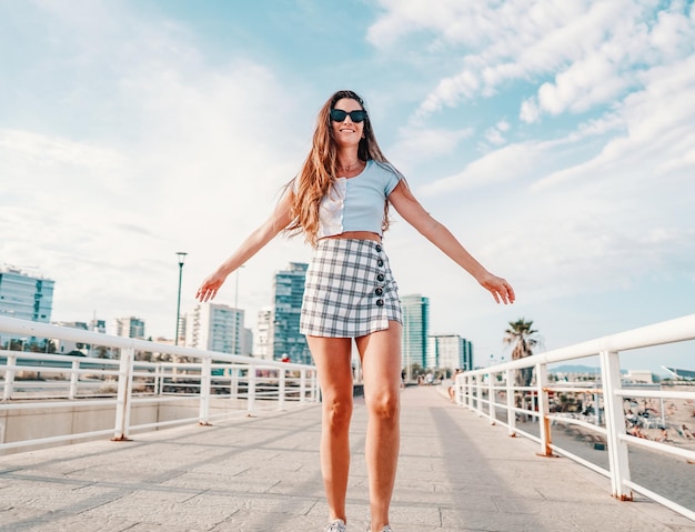 Beautiful young fashionable woman in sexy stylish clothes posing in the modern city with skyscrapers on background