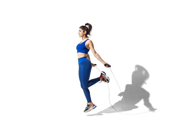 Beautiful young female athlete practicing on white studio background with shadows