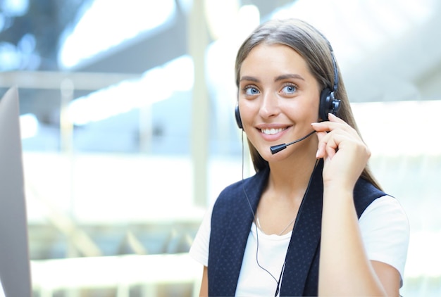 Beautiful young female call center operator with headset in office.