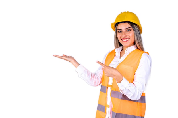 Beautiful young female engineer wearing safety gear pointing to the side on white background