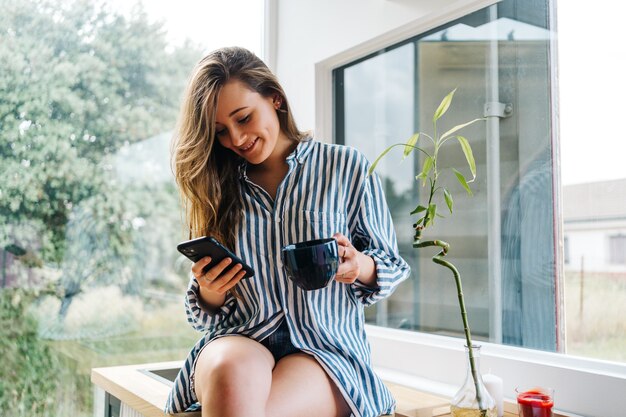 beautiful young female siting on kitchen counter and browsing on mobile phone i modern kitchen