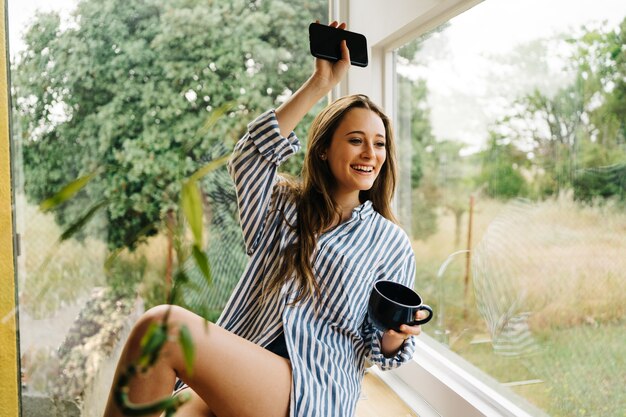 beautiful young female siting on kitchen counter and browsing on mobile phone i modern kitchen