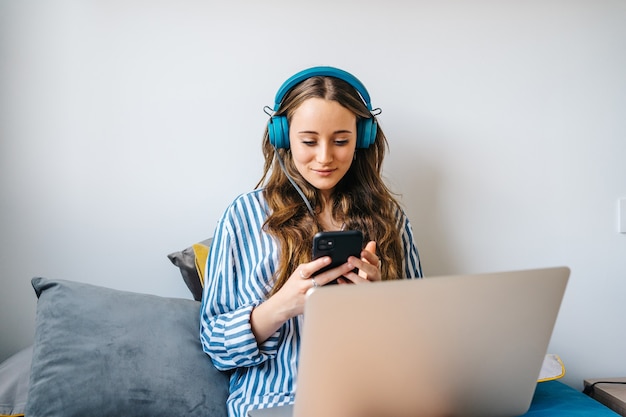 beautiful young female with headphones working remotely and browsing on her mobile phone