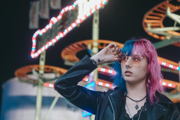 Beautiful young female with sunglasses and a leather jacket in front of illuminated amusement park