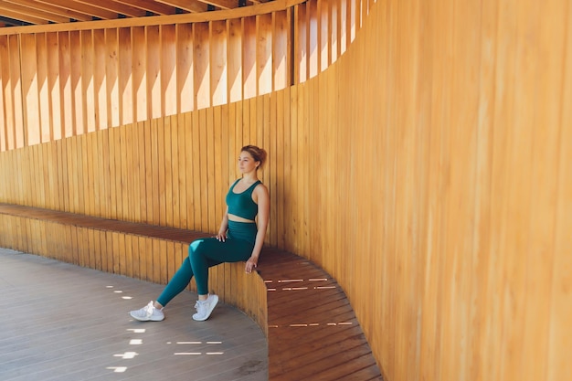 Beautiful young fitness instructor gives lessons on video using laptop on a wooden veranda on the street