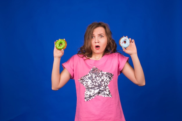 Beautiful young funny girl with donuts on blue.