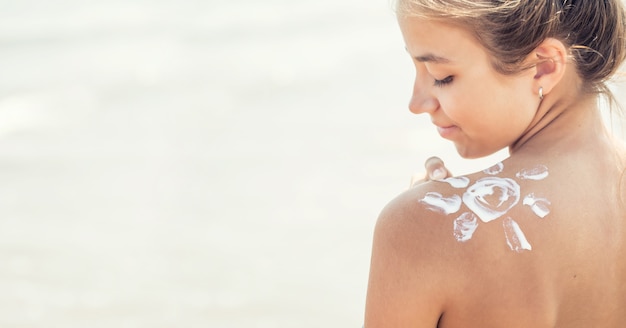 Beautiful young girl applying sunscreen on her shoulder on the beach.