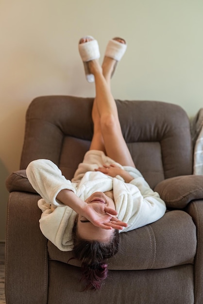 Beautiful young girl in a bathrobe and sneakers lies on a chair upside down and relaxes in his spare time. Relaxation concept