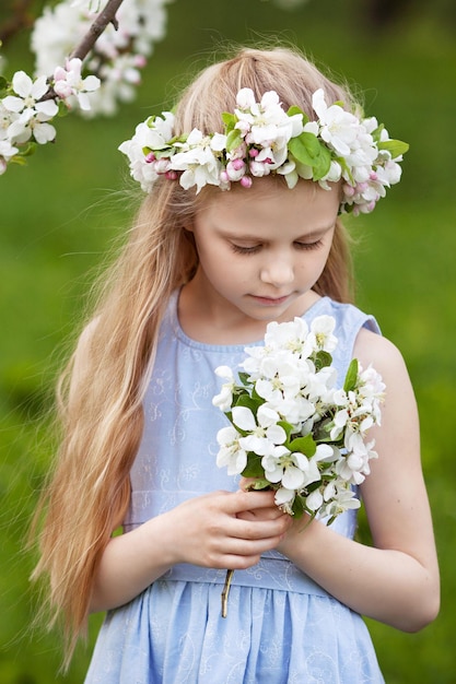 Beautiful young girl in blue dress in the garden with blosoming apple trees Cute girl holding a bouquet of flowers