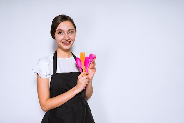 Beautiful young girl cook in black apron likes to cook food holds tools for baking