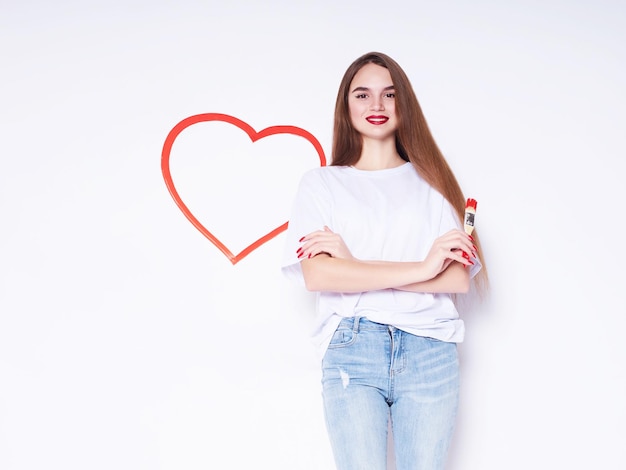 A beautiful young girl draws a heart on the wall. Love concept. beautiful smiling young woman. Gift for Valentine's Day. Isolated on white background.