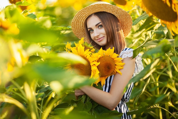 Beautiful young girl enjoying nature on the field of sunflowers at sunset