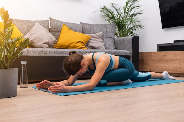 Beautiful young girl goes in for sports on a gymnastic mat at home