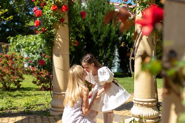 Beautiful young girl and her mom on a background of red roses Rose Garden Concept of happy family