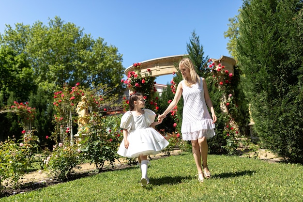 Beautiful young girl and her mom on a background of red roses Rose Garden Concept of happy family