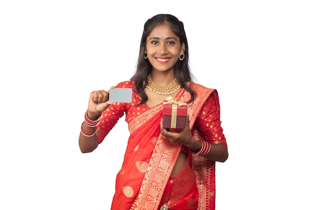 Beautiful young girl holding and posing with a gift box with a credit or debit card on a white background