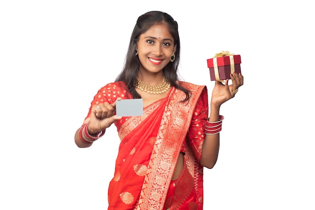 Beautiful young girl holding and posing with a gift box with a credit or debit card on a white background