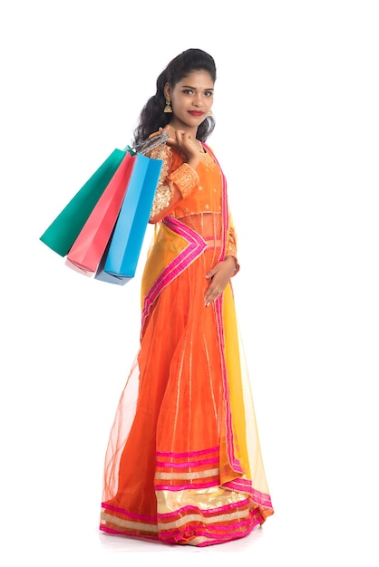 Beautiful young girl holding shopping bags while wearing traditional ethnic wear on white