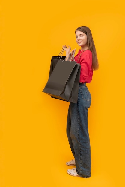 Beautiful young girl holds black paper bags after shopping on yellow background Black Friday Concept Vertical frame