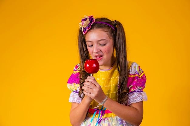 Beautiful young girl in June party clothes eating Love Apple Apple dessert covered in red caramel