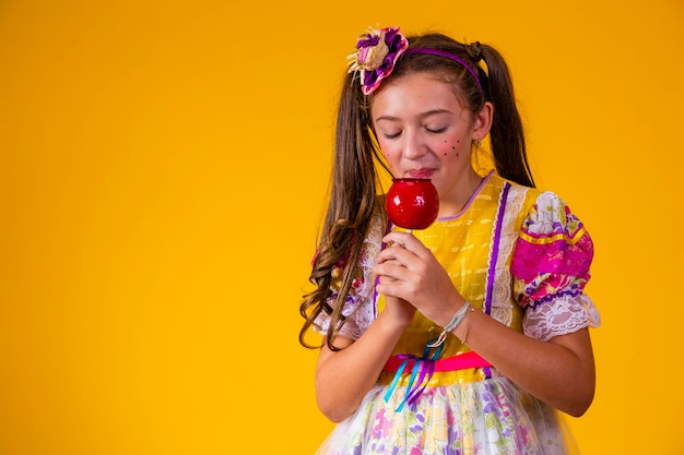 Beautiful young girl in June party clothes eating Love Apple Apple dessert covered in red caramel