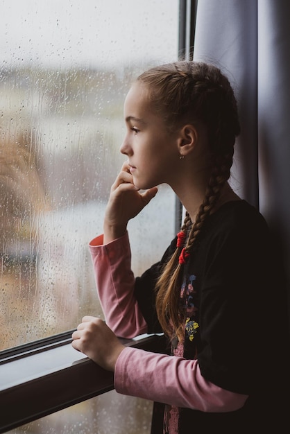 A beautiful young girl looks out the window with rain and dreams Rain Autumn Atmosphere