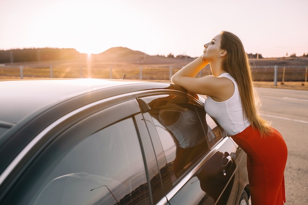 Beautiful young girl near a car in the evening in the sunset sun in an empty parking lot