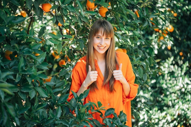 Beautiful young girl in orange dress is smiling by showing perfect gestures in orange garden