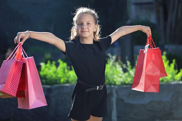 Beautiful young girl in the park holds colored bags in outstretched hands